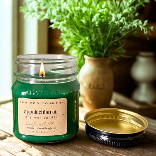A 7.5 oz mason jar candle that is lit, green in color, and sitting on a countertop.