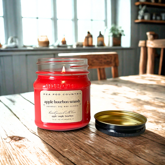 A lit 7.5 oz mason jar candle that is apple red in color sitting on a kitchen table.
