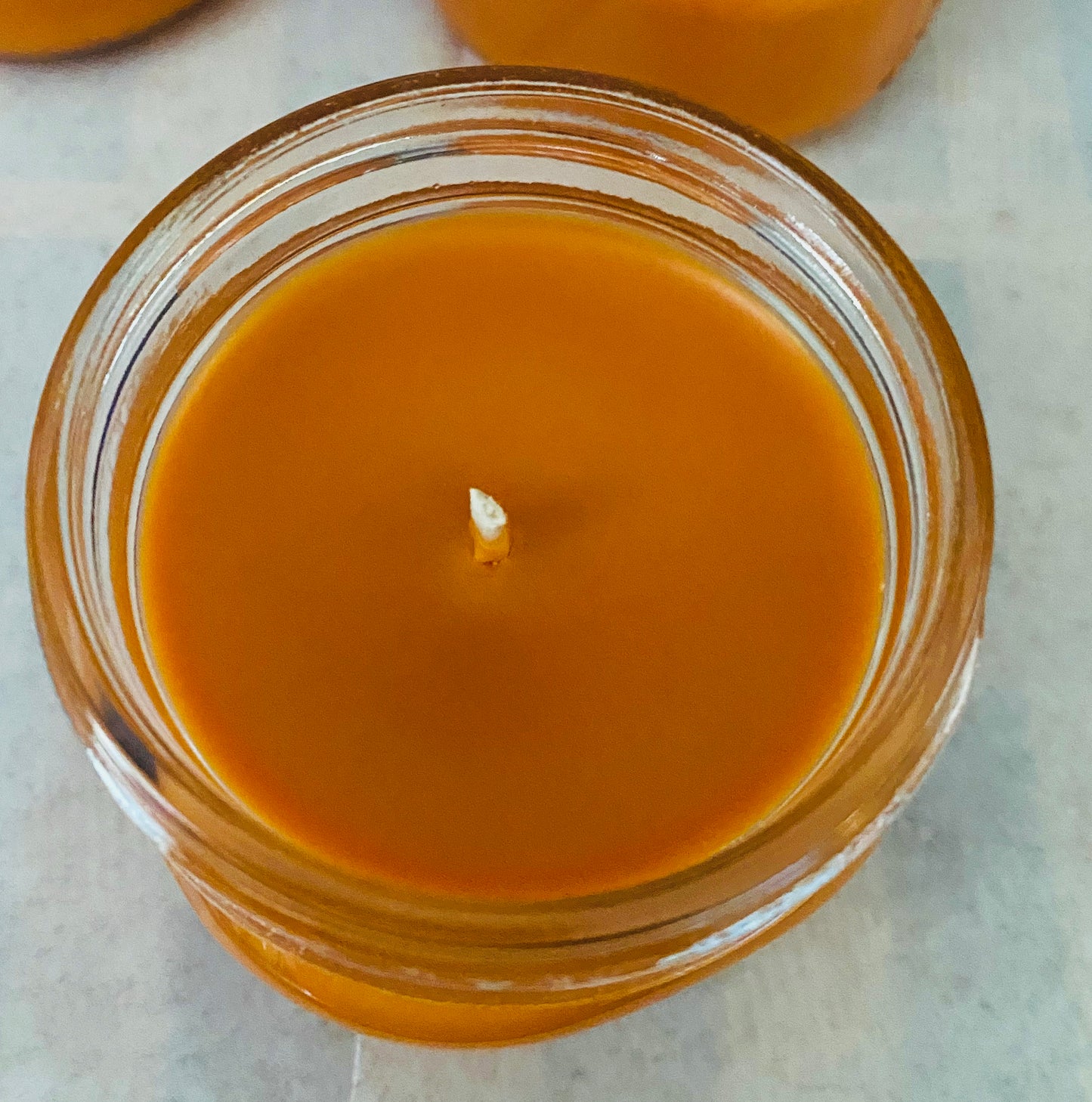 A view of the top of an unlit mason jar candle showing smooth soy wax and a cotton wick.