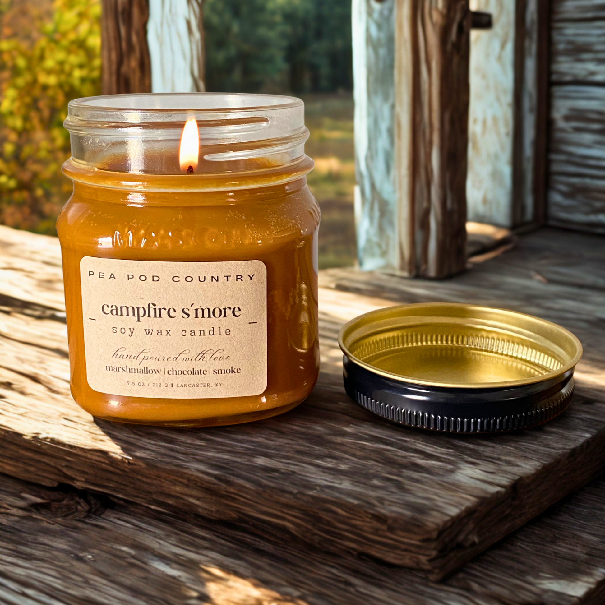 A lit 7.5 oz mason jar candle that is graham cracker brown in color sitting on an outdoor bench. 