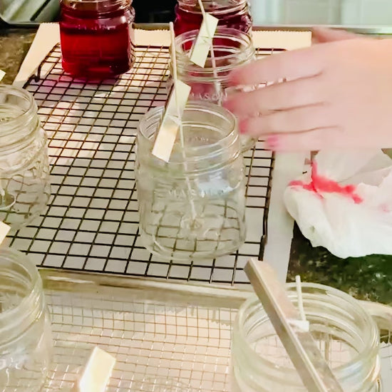 The process of hand pouring 7.5 oz mason jar candles. Red in color. 